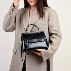 Détail du sac à main en cuir verni noir avec boucle métallique sur un blazer kaki chic