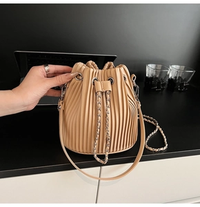 Detail of beige pleated drawstring bucket bag with metal chain and PU leather texture