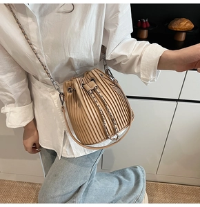 Side view of a beige pleated bucket bag with metal chain strap on a female model