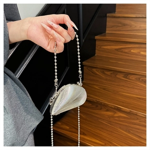 Detail of silver shell-shaped acrylic clutch bag with bead chain on wooden stairs
