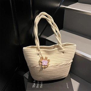 Chic woven beach tote bag with a floral butterfly charm on a minimalist stone background