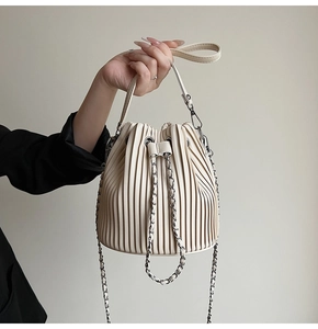 Detailed view of beige pleated bucket bag with metal chain strap and fine stitching