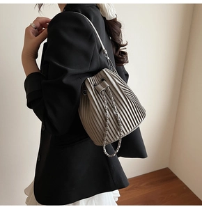 Detail of taupe pleated bucket bag with metal chain drawstring and accordion texture