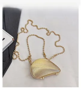 Detail view of a shell-shaped gold evening clutch bag with beaded metal chain on a white fabric