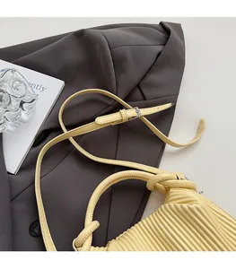 Close-up of light yellow pleated handbag featuring a slim shoulder strap and silver buckle