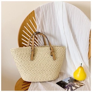 Beige woven straw tote bag with brown faux leather handles on a wooden chair