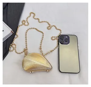 Detailed top view of a mini gold shell evening clutch next to a smartphone for size reference