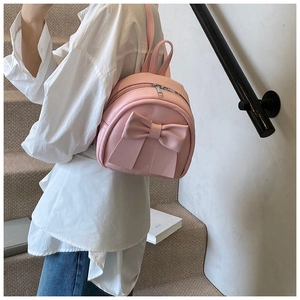 Lifestyle shot of a mini pink bow backpack on a model in a minimalist setting