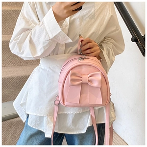 Close-up of a pink mini backpack with large bow detail held by a model in a street setting