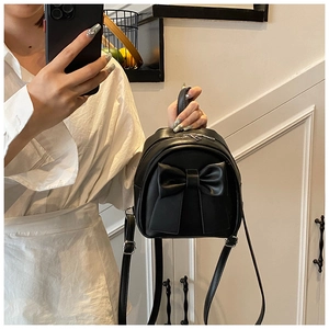 Detail of a black mini backpack featuring a large 3D bow and silver metal zippers