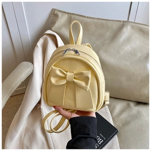 Detail of pale yellow mini backpack with large bow and dual zipper closure shown in hand