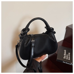 Detail of black vertical pleated handbag with soft synthetic leather texture and top handle