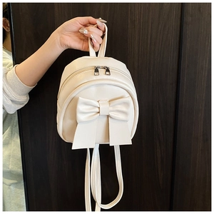 Detail of cream mini backpack featuring a large bow and silver dual metal zippers