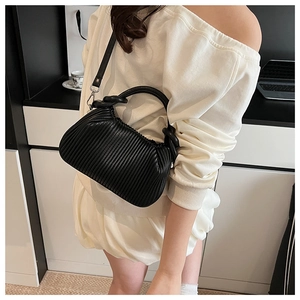 Detailed view of black pleated handbag with vertical texture and detachable metal hooks