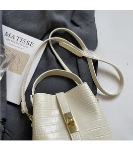 Detail of crocodile embossed cream bucket bag with gold twist lock and adjustable strap