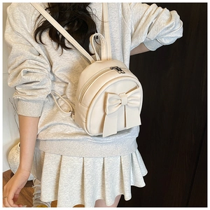 Rear view of a model wearing a mini cream backpack with a large bow detail