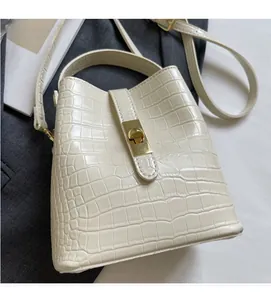 Close-up of beige bucket bag with crocodile texture, gold metal lock and stitching details
