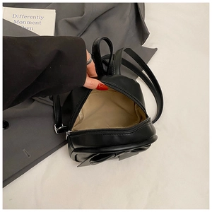 Detail of black leather backpack with bow showing beige inner lining and zipper closure