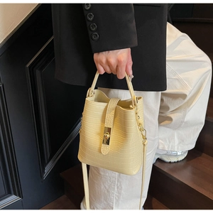 Detail of pale yellow crocodile texture bucket bag with golden twist lock buckle