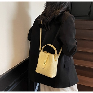 Detail of yellow crocodile embossed bucket bag featuring a gold lock and adjustable strap
