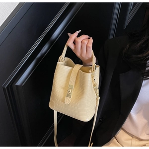Detail of beige crocodile embossed bucket bag with gold square lock and leather strap