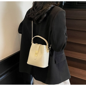 Detail of cream crocodile embossed bucket bag with gold clasp shown on a model's arm