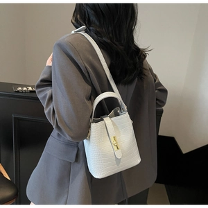 White crocodile pattern bucket bag with metal lock shown as a stylish crossbody on model