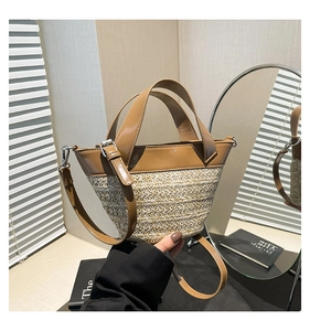 Detail of woven straw and caramel PU leather bucket bag with dual handles and strap