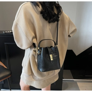 Detailed view of black crocodile pattern bucket bag with gold hardware on a model
