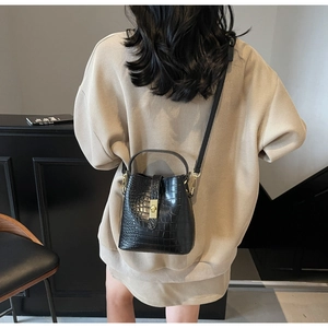 Rear view of a model wearing a black croc-embossed bucket bag with gold lock and strap