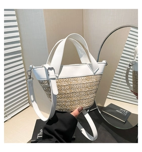 Detail of woven straw bucket bag with white leather trim and adjustable shoulder strap