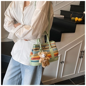 Close-up of striped woven shoulder bag featuring green leather trim and cute bear charm