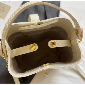 Detail view of cream white bucket bag with crocodile texture and gold metal hardware