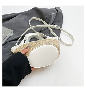 Detail of woven straw bucket bag with white leather trim and adjustable shoulder strap