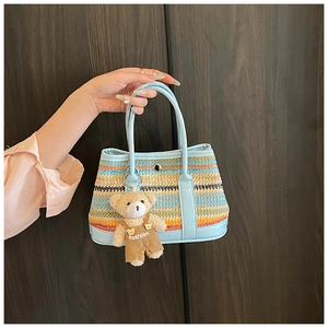 Detail of colorful striped woven tote bag with light blue handles and a teddy bear charm