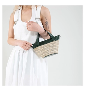 Detailed close-up of woven straw texture and dark green leather trim on bucket bag