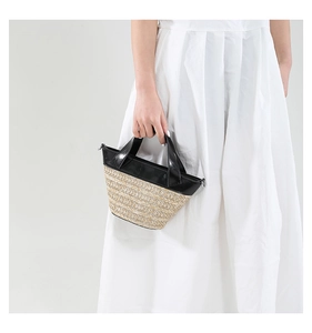 Detail of woven straw bucket bag with black leather handle held by model in white dress