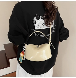 Detail of cream glossy saddle bag with pearl doll charm worn on shoulder