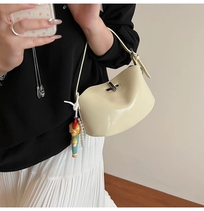 Close-up of cream half-moon handbag with silver twist lock and pearl doll charm detail