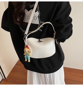 Detail of cream-colored glossy half-moon crossbody bag with cute cartoon doll charm