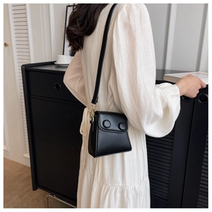 Détail d'un mini sac bandoulière noir avec boutons décoratifs porté sur une robe blanche