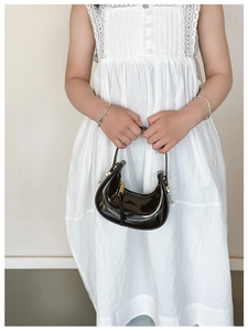 Detail of a mini black patent leather crescent handbag with elegant gold hardware