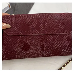 Detail of burgundy snakeskin leather texture and gold chain strap on flap bag