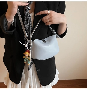 Detail of light blue glossy handbag with metal turn-lock and pearl chain accessories