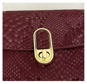 Close-up of burgundy snake-patterned leather texture and golden woven turn-lock closure