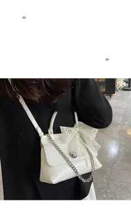 Détail d'un sac bandoulière blanc brillant avec un nœud en dentelle et une chaîne argentée