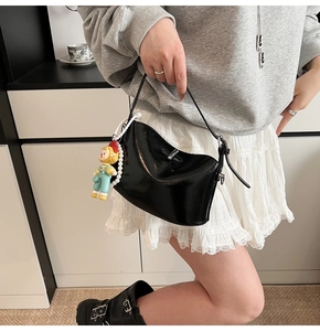 Detail of black patent leather underarm bag with pearl chain and cartoon charm