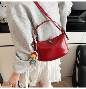 Close-up of red glossy leather handbag with silver clasp and decorative pearl keychain