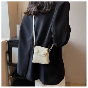 Détail d'un mini sac bandoulière crème porté sur un blazer noir pour un look moderne