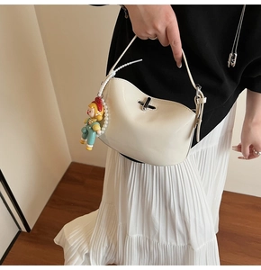 Close-up of a glossy creamy white shoulder bag featuring a silver clasp and pearl charms